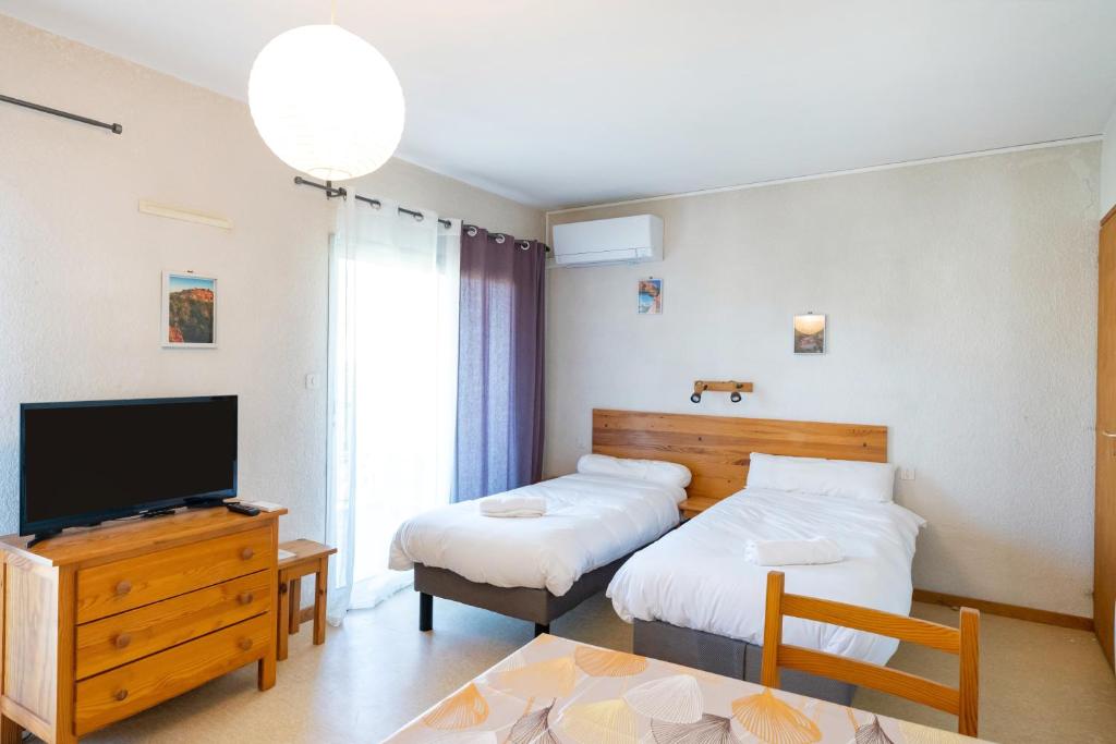 a bedroom with two beds and a tv and a table at Les Mimosas - Appartement 09 in Cazaubon