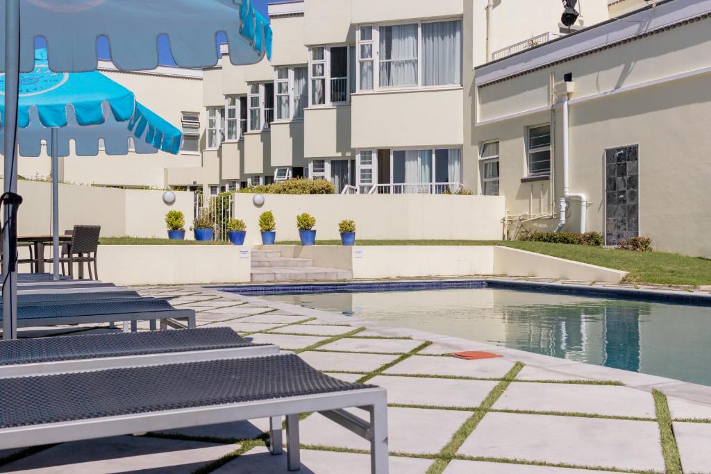 ein Schwimmbad mit Liegestühlen und Sonnenschirmen neben einem Gebäude in der Unterkunft The Beach Hotel in Port Elizabeth