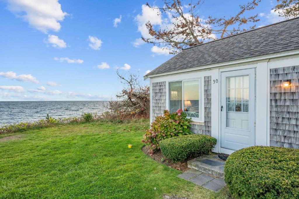 a small house with a white door and the ocean at Oceans Edge: Drift, Dream, Repeat in South Yarmouth