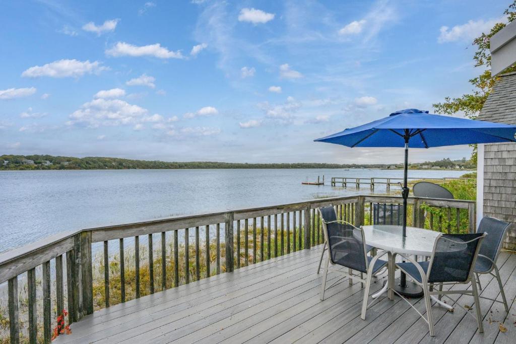 a table and chairs on a deck with a blue umbrella at Peaceful Covefront Cottage Retreat in Eastham in Eastham