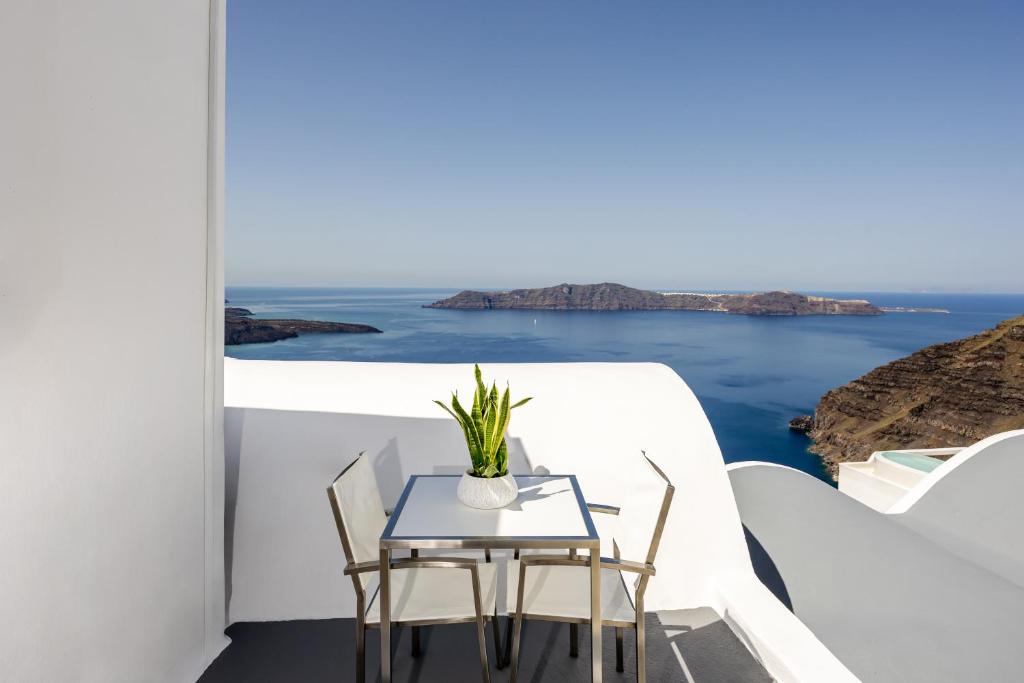 a table and chairs on a balcony with a view of the ocean at Caldera Jewel Santorini in Firostefani
