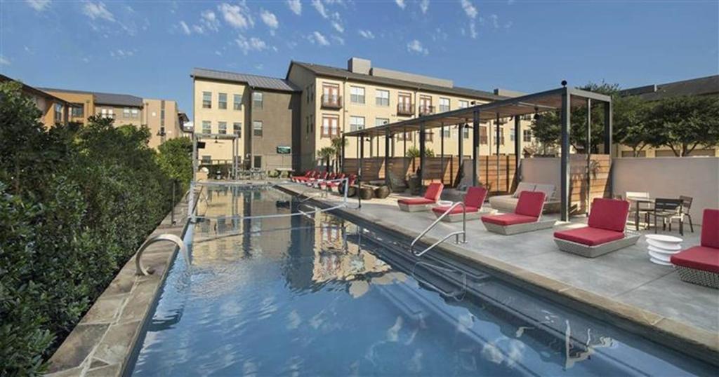 a swimming pool with red chairs and a building at King Aqua Suite Walkable Legacy West King Bed, Pool & Gym in Plano