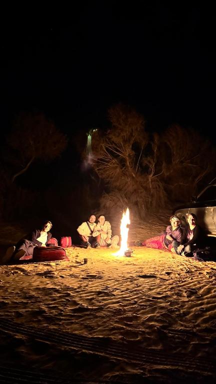 a group of people sitting around a fire on the beach at night at Leen Luxury Camp in Disah