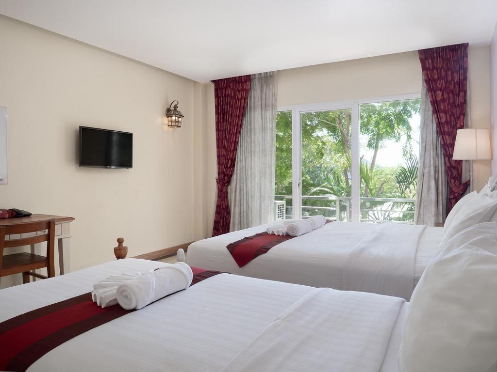 zwei Betten in einem Hotelzimmer mit Fenster in der Unterkunft อัมพวารี Amphawaree Hotel in Samut Songkhram