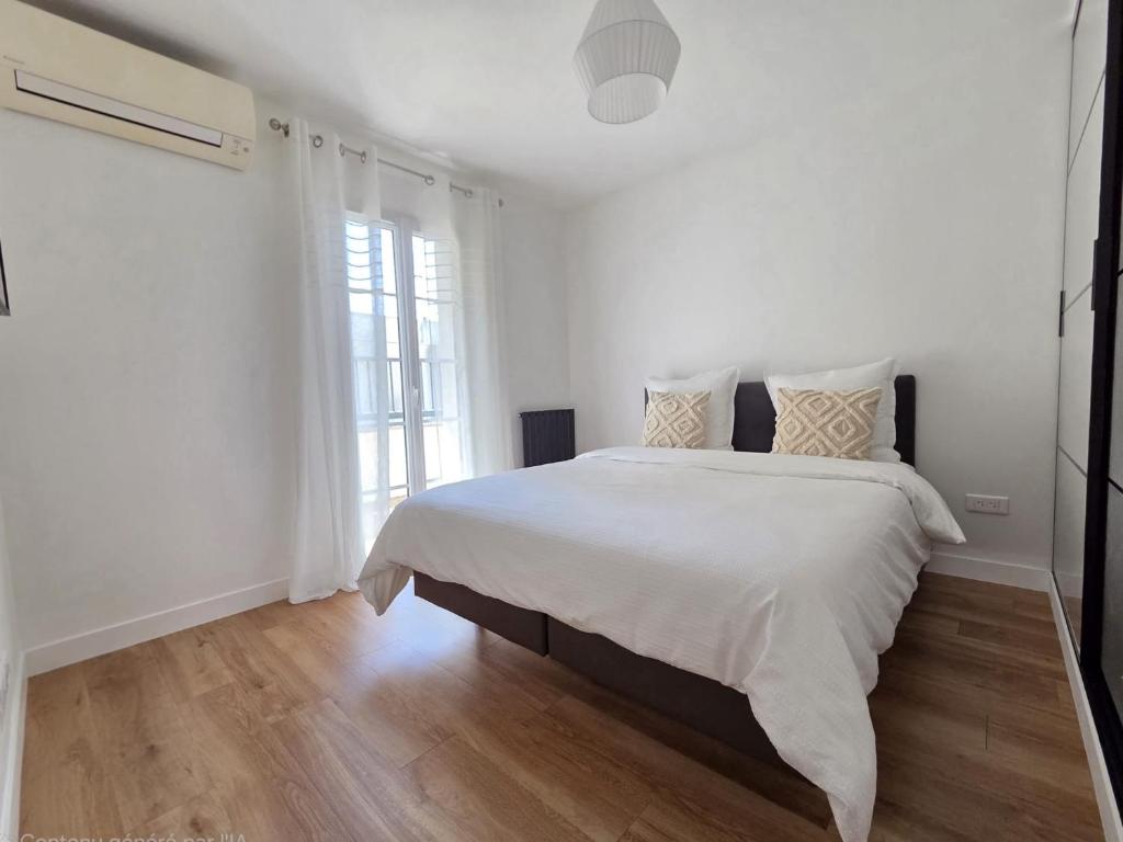a white bedroom with a large bed and a window at Appartement Dora in Villiers-sur-Marne