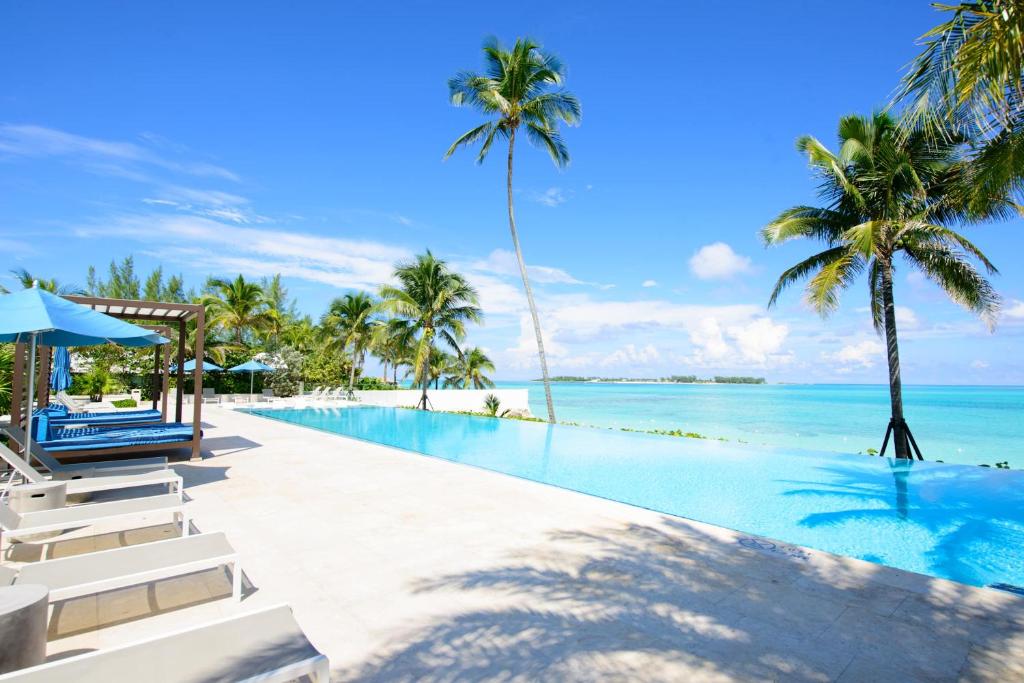 a swimming pool with palm trees and the ocean at Garden Villa Condo at ONE Cable Beach in Nassau