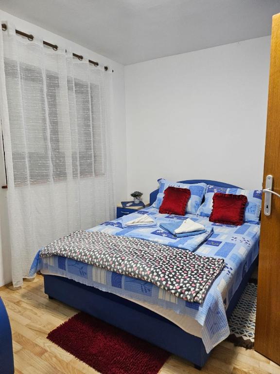 a bedroom with a bed with blue sheets and red pillows at Apartman Ceca in Lepterija