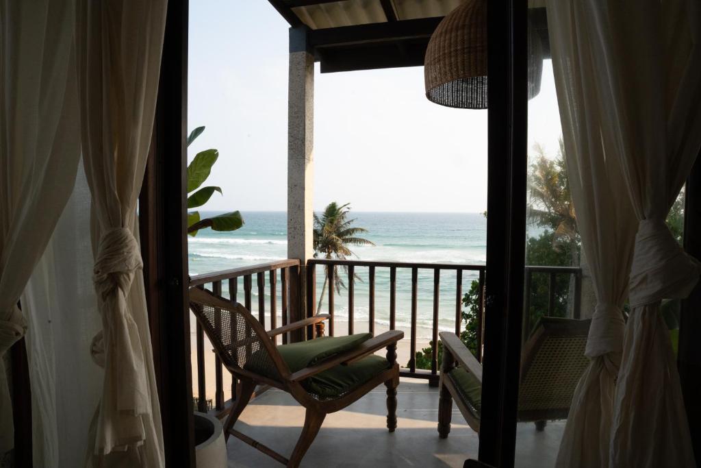 a room with a balcony with a chair and the ocean at Ahangama Surf Club in Ahangama