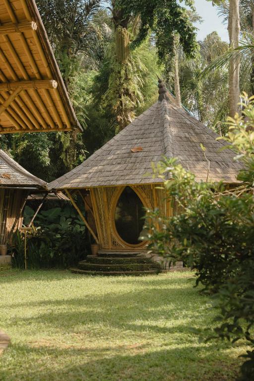 a small house with a thatched roof in the grass at The Kul Kul Farm in Bringkit