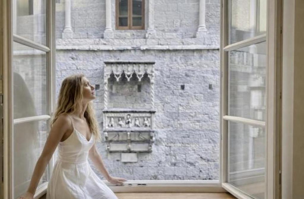 a woman in a white dress looking out of a window at Amazing San Lorenzo 19 Apt with Private Parking in Genoa