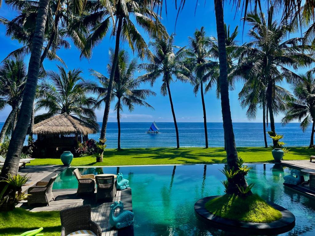a resort pool with palm trees and the ocean at Louka Beach Bali in Tianyar