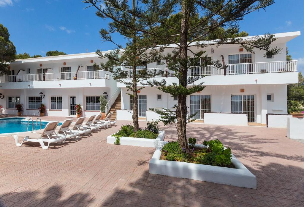 un grande edificio bianco con sedie a sdraio e piscina di Hostal Es Pi - Emar Hotels a Playa Migjorn