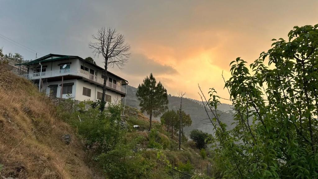a house on the side of a hill with a sunset at AtulyaNeer Lakeview Cottage in Kanatal