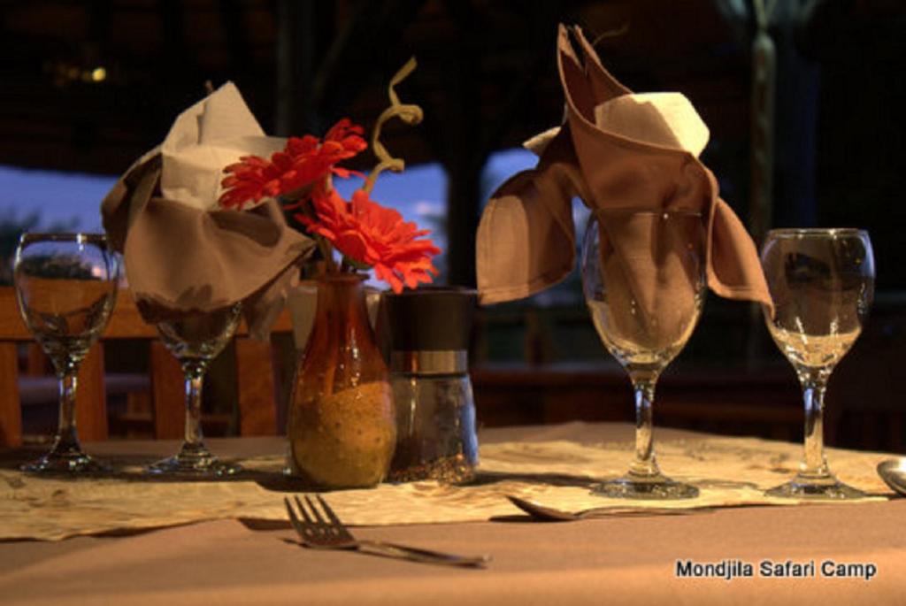 una mesa con copas de vino y flores rojas. en Mondjila Safari Camp, en Okaukuejo