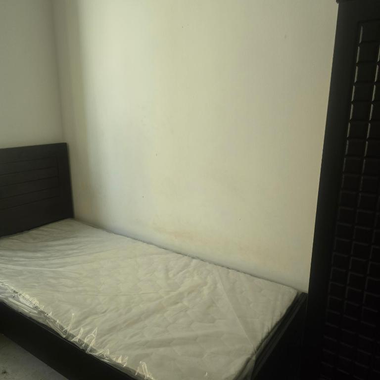 a small bed in a corner of a room at Bedroom with shared kitchen men only in Sharjah