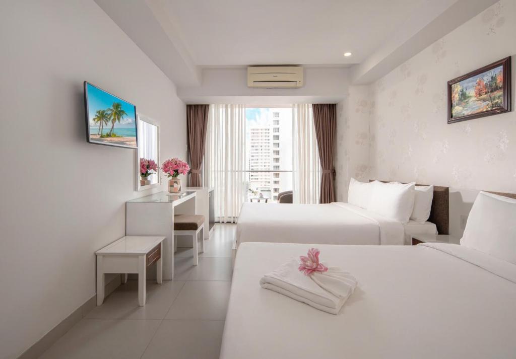 a white hotel room with two beds and a window at Sophia Central Nha Trang Hotel by HT in Nha Trang