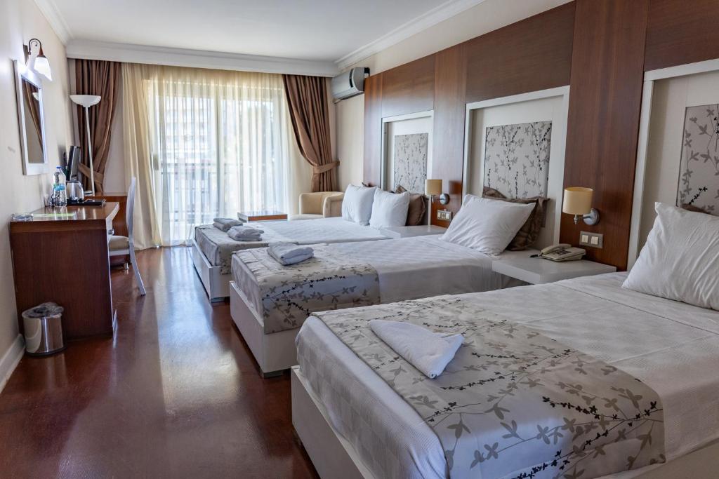 a hotel room with three beds and a desk at Sentinus Beach Hotel in Kuşadası