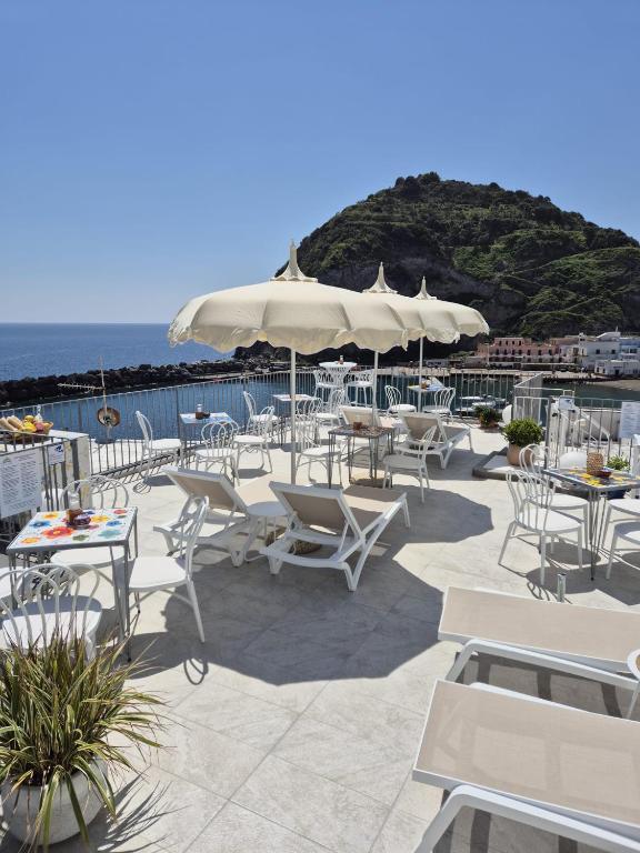 a patio with white chairs and tables and umbrellas at Casa Borgo Sant'Angelo in Sant'Angelo D'Ischia