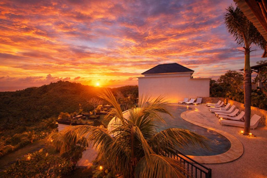 a sunset over a resort with a pool and palm trees at Kelingking Parama Resort in Nusa Penida