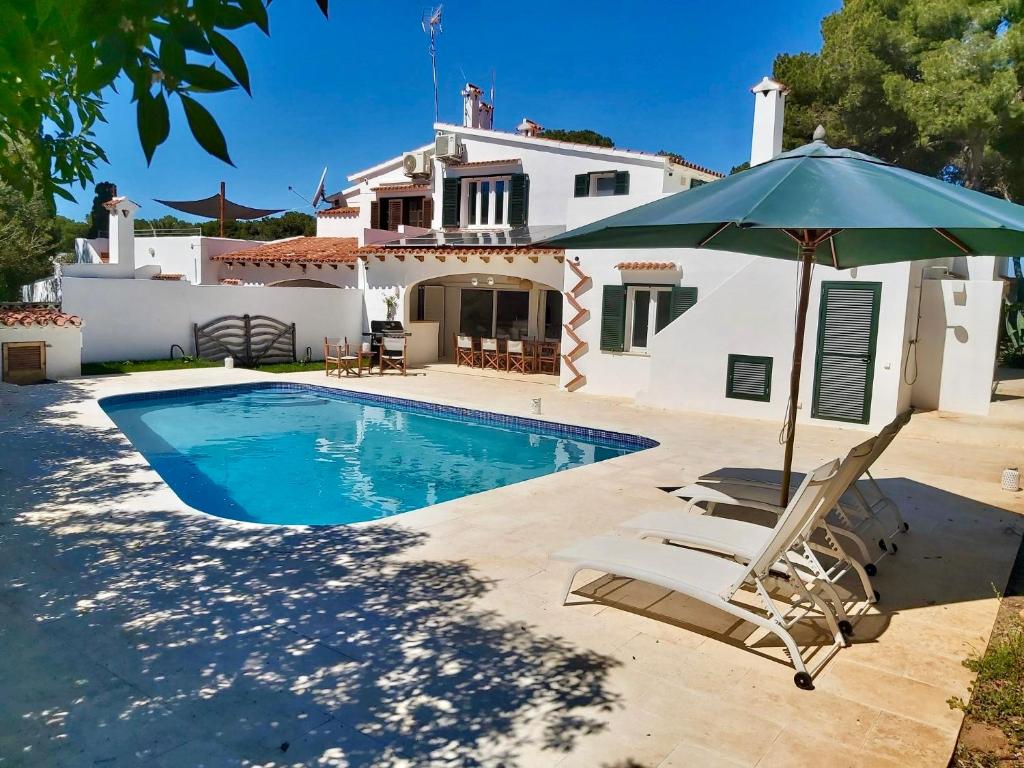 a villa with a swimming pool and an umbrella at Los Caballos Villa in Cala Galdana
