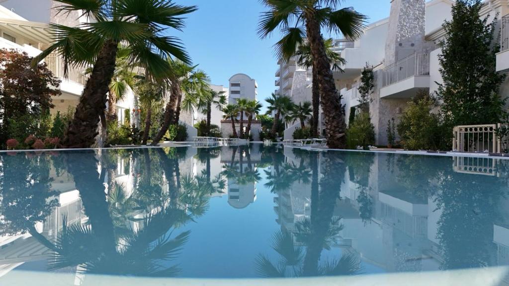 a swimming pool with palm trees and buildings at VELORA STAYS Florinas in Lido di Jesolo