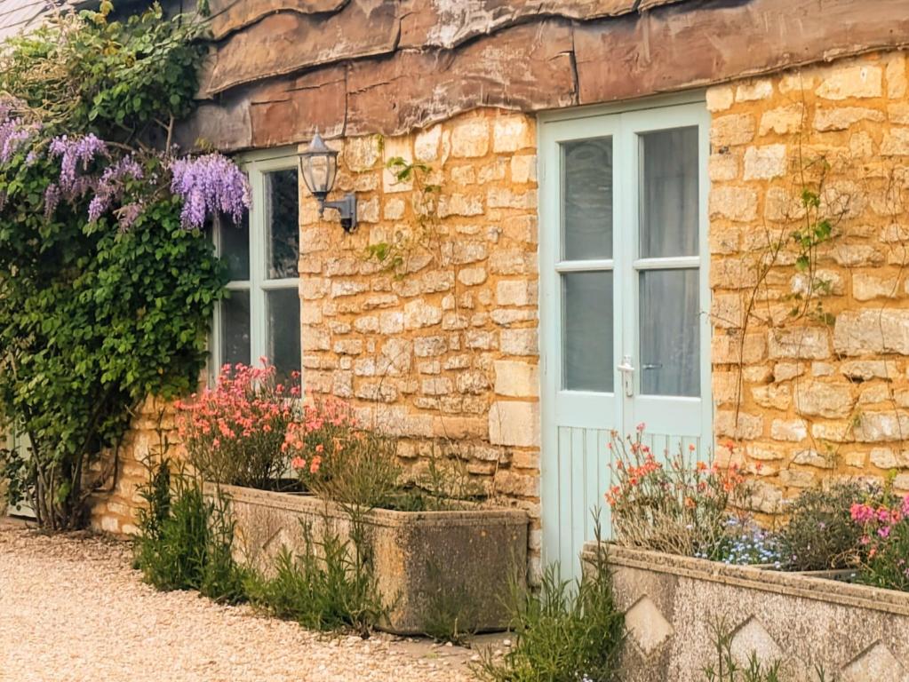 a stone house with a white door and flowers at South Cotswolds cottage in Great Somerford