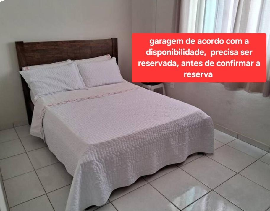 a bed with a white comforter and a red sign at Quarto privado com ar condicionado in Governador Valadares