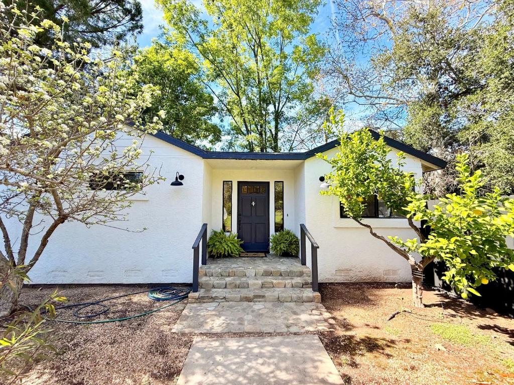 a white house with a black door and trees at Charming Private Cottage in Ojai in Ojai
