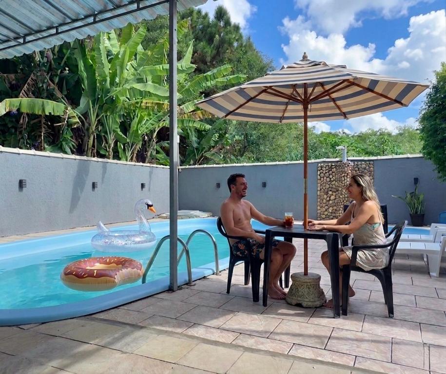 a man and woman sitting at a table next to a pool at Rede Elevare Ilha do Sol in Florianópolis