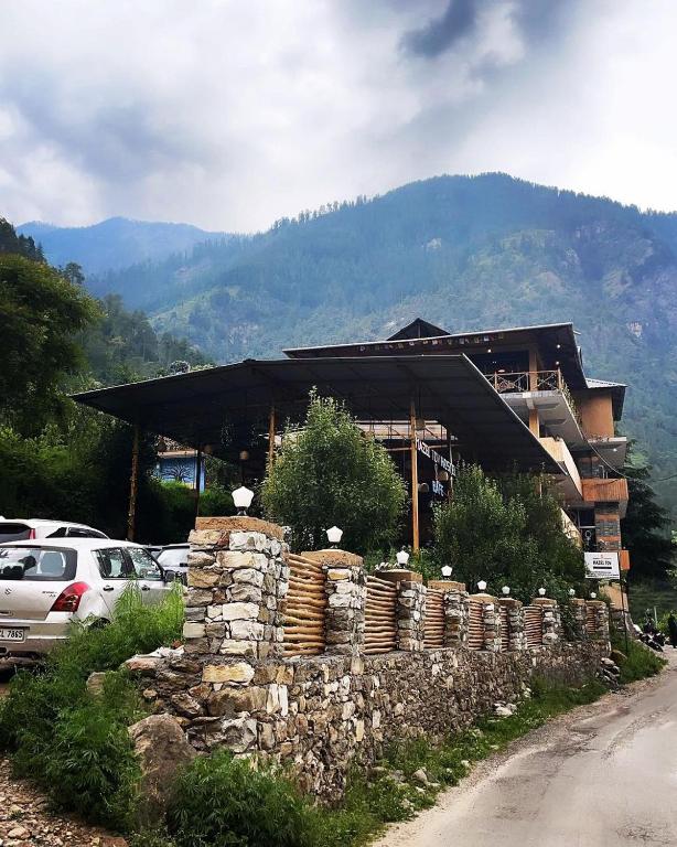 a building with a stone wall next to a road at Mazel Tov Stays, Tirthan Valley in Gushaini