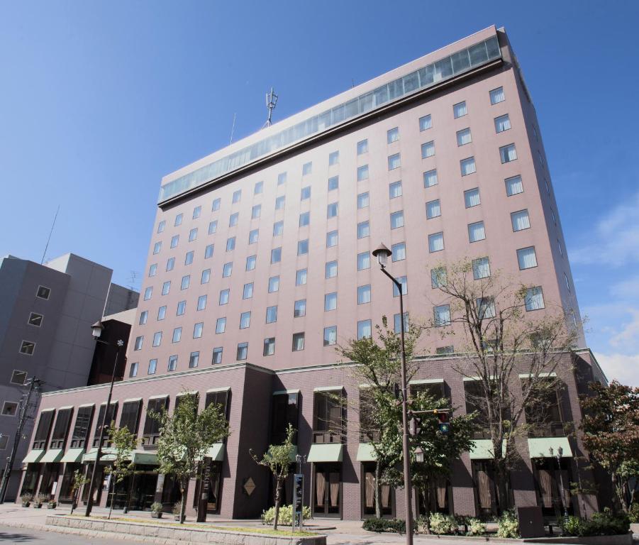 un gran edificio blanco con árboles delante de él en Hotel Crescent Asahikawa, en Asahikawa