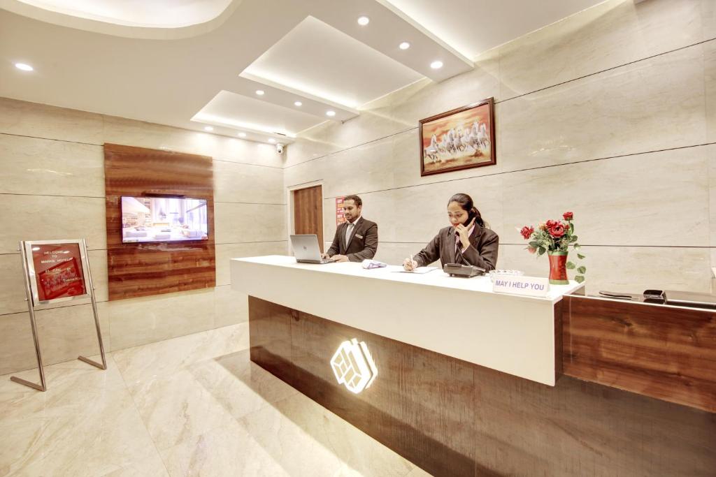 zwei Personen sitzen an einem Rezeptionstresen in einer Lobby in der Unterkunft Marks in Noida