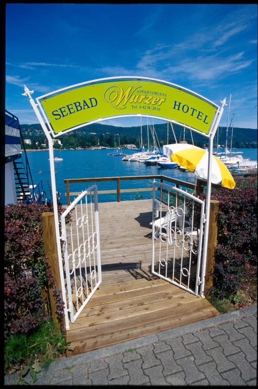 a wooden boardwalk with an umbrella and a hotel at Hotel Garni Wurzer in Velden am Wörthersee