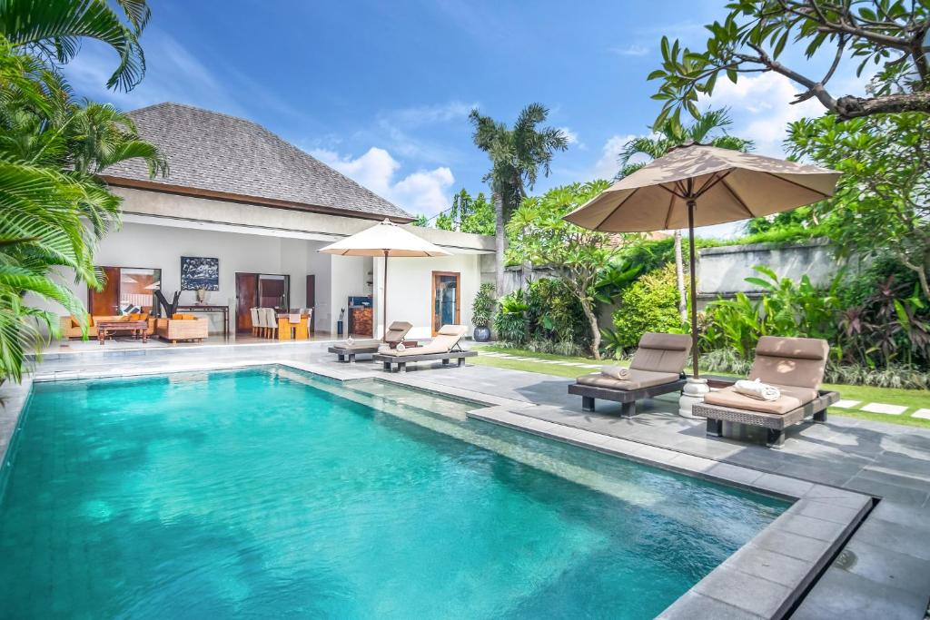a swimming pool in a villa with chairs and an umbrella at Serene Villas in Seminyak