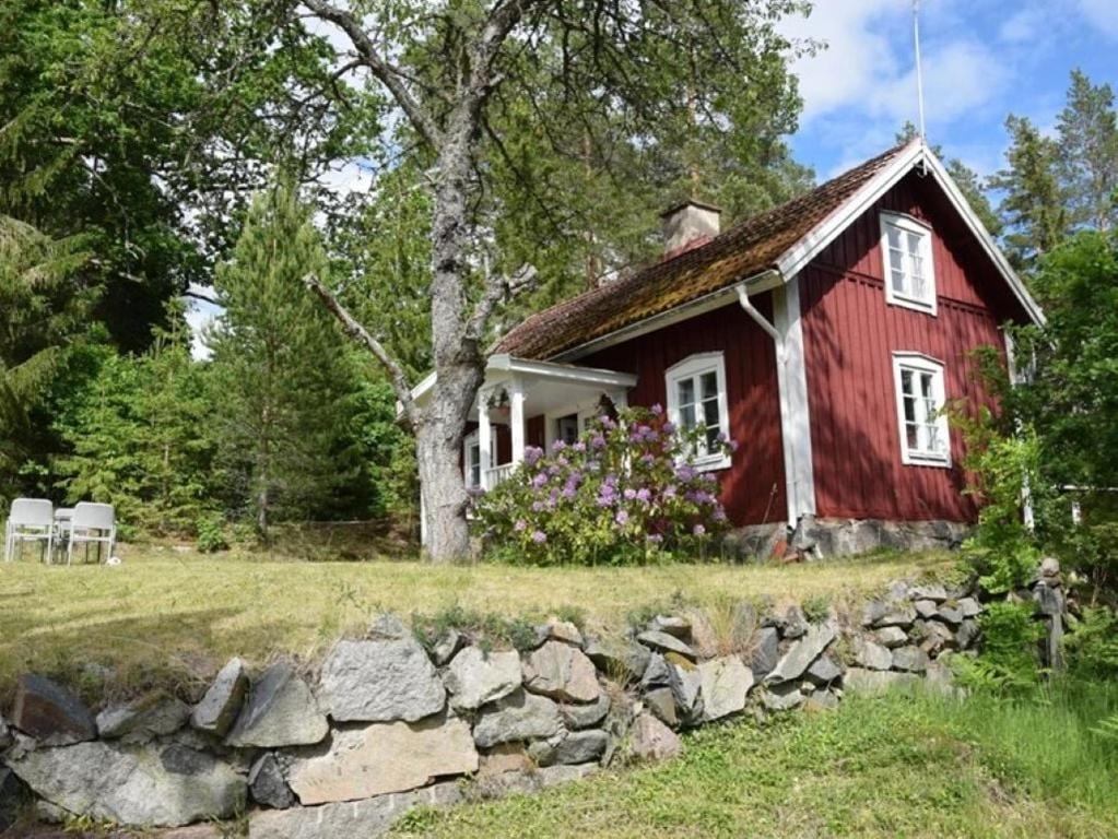 a red house with a stone wall in front of it at Cozy farmhouse with rowboat! in Skönberga