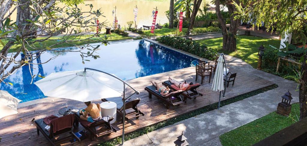 a group of people sitting under an umbrella by a pool at Lanna Dusita Riverside Boutique Resort in Chiang Mai