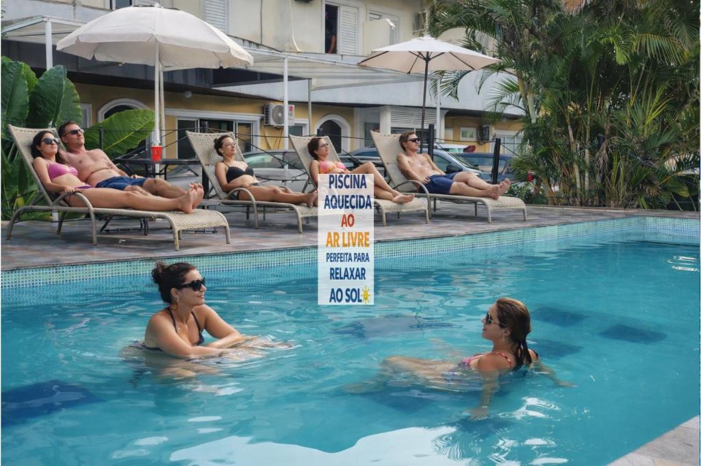 Eine Gruppe von Menschen in einem Schwimmbecken mit einem Schild im Wasser in der Unterkunft Hotel Pousada Iracemar, 60m da Praia da Enseada, Piscina Aquecida ao Ar Livre para Relaxar em Qualquer Estação, Café da Manhã, Estacionamento, Recepção 24h, Aproveite o Mar, Passeios e Atividades Náuticas a 100 metros in Guarujá