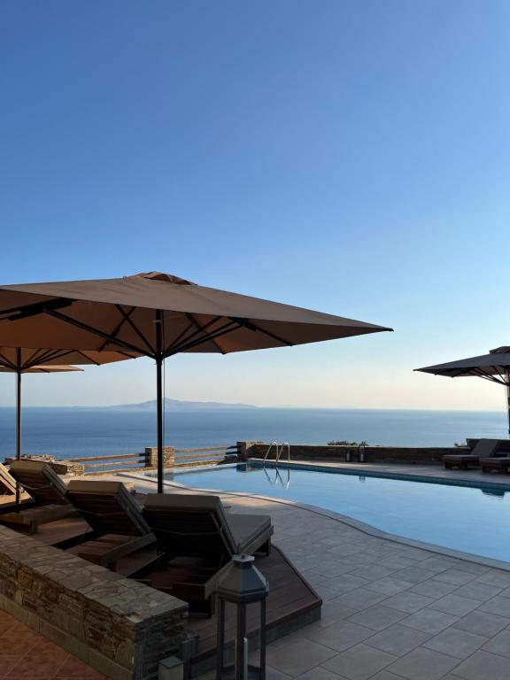 ein Pool mit Liegestühlen und Sonnenschirmen direkt am Meer in der Unterkunft August Andros in Ándros