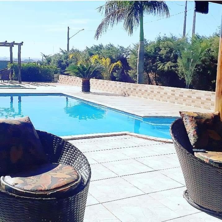 a swimming pool with two wicker chairs next to it at Recanto Barretos in Barretos