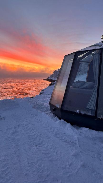 a building sitting in the snow with the sunset in the background at Aurora Sea Lodges AURORAHUT in Herjenes