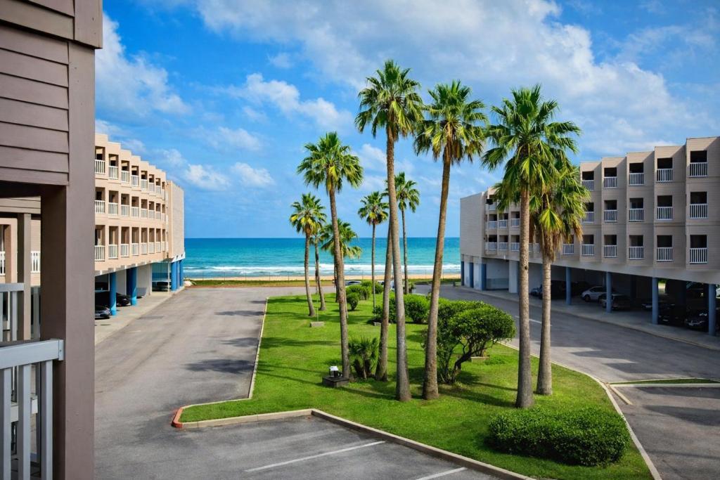 a view of the beach from the balcony of a hotel with palm trees at The Sandbar Stay - North Beach Waterfront Condo in Corpus Christi