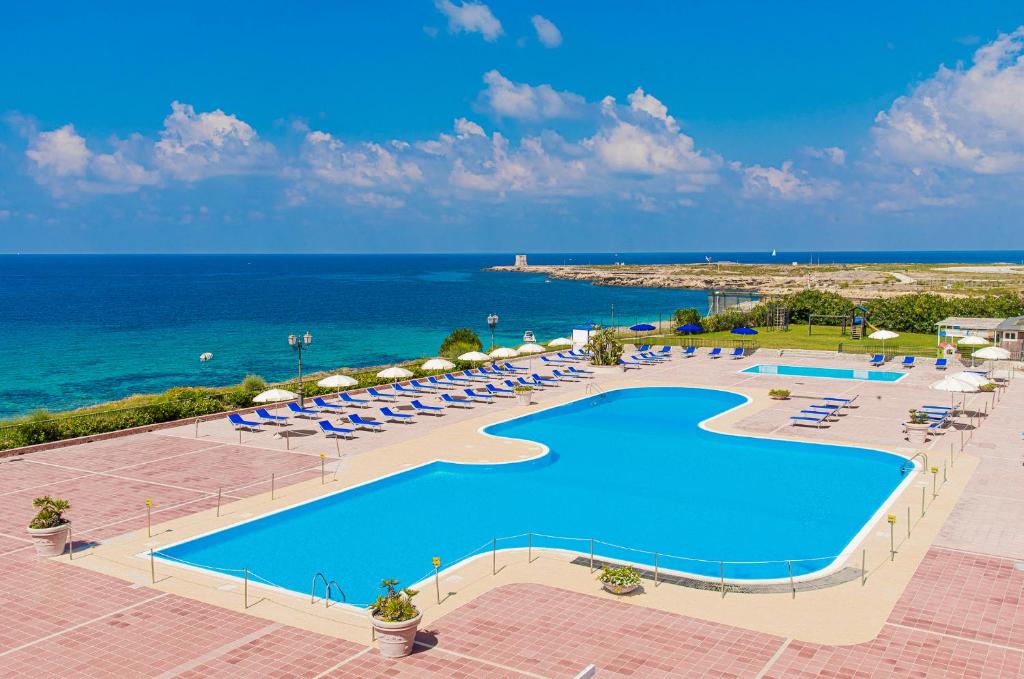 a swimming pool with chairs and umbrellas and the ocean at VOI Florio Resort in Cinisi