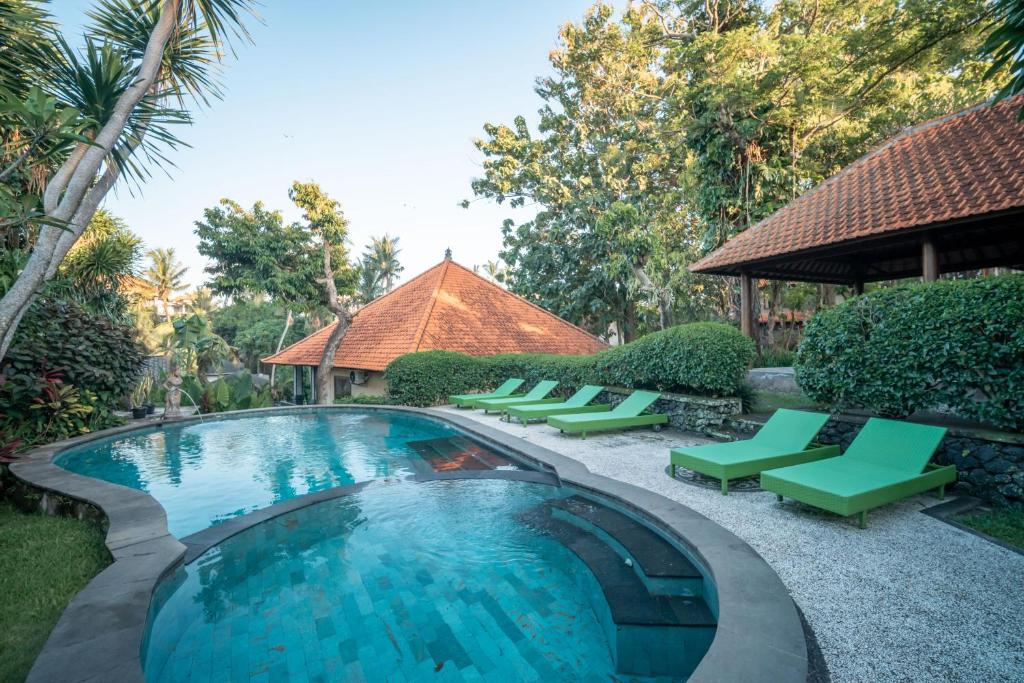 a swimming pool with green chairs and a building at Argasoka Bungalows in Ubud