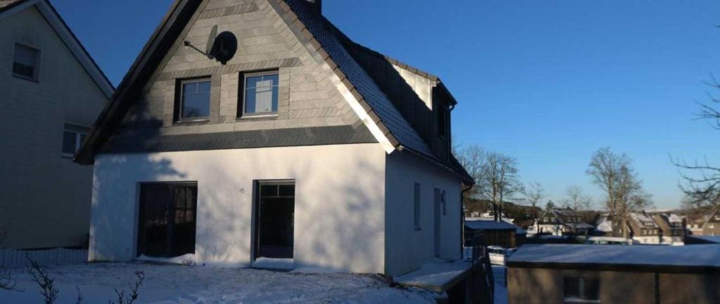une maison blanche avec un toit noir dans la neige dans l'établissement Ferienhaus Familienglück, à Winterberg