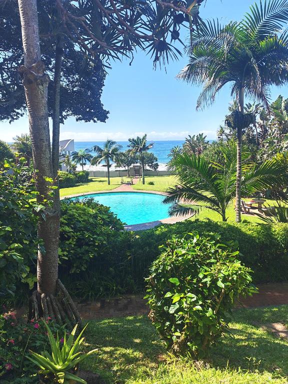 a swimming pool with palm trees and the ocean at OceanFront- Whale Watch- On Beach- Stunning in Umdloti
