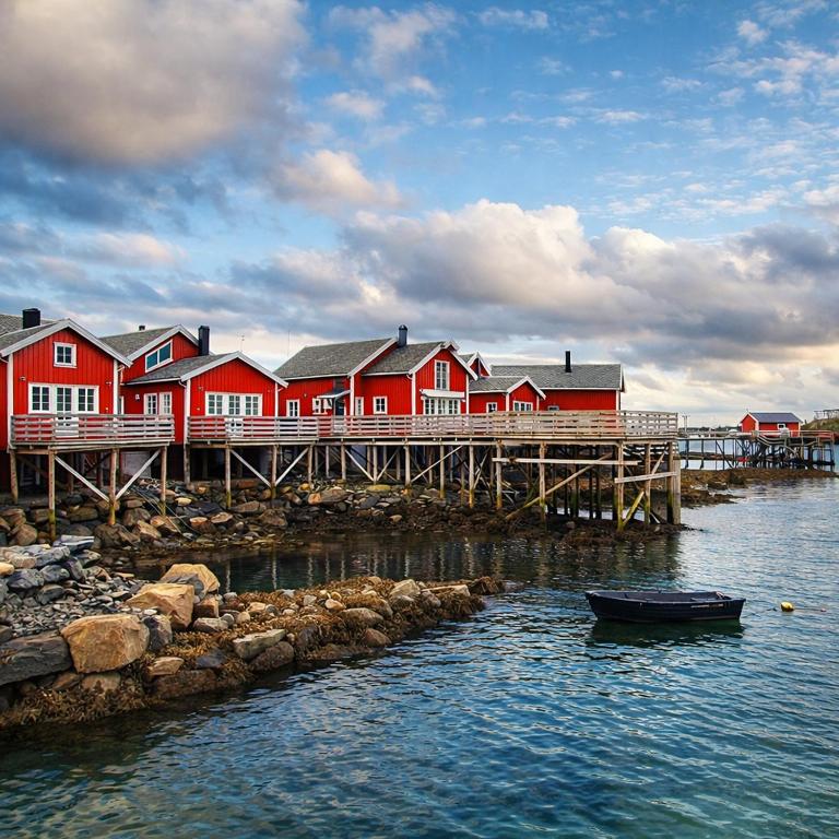 a dock with red houses and a boat on the water at Andøy Vest Rorbuer Reine in Reine