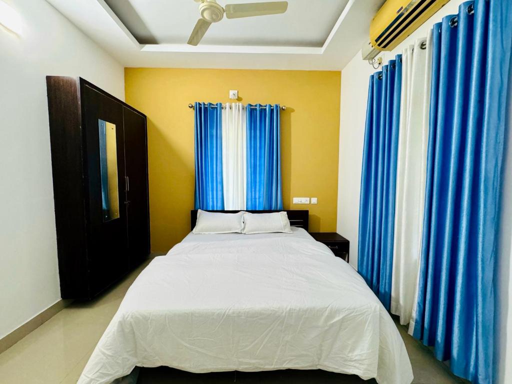 a bedroom with a white bed with blue curtains at two bedroom anandha vibes in Guruvāyūr