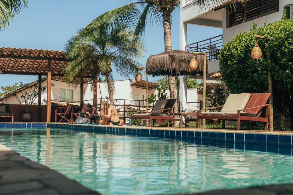 a swimming pool with people sitting in chairs next to a house at Pipa Panorama Flats&Apartamentos in Pipa
