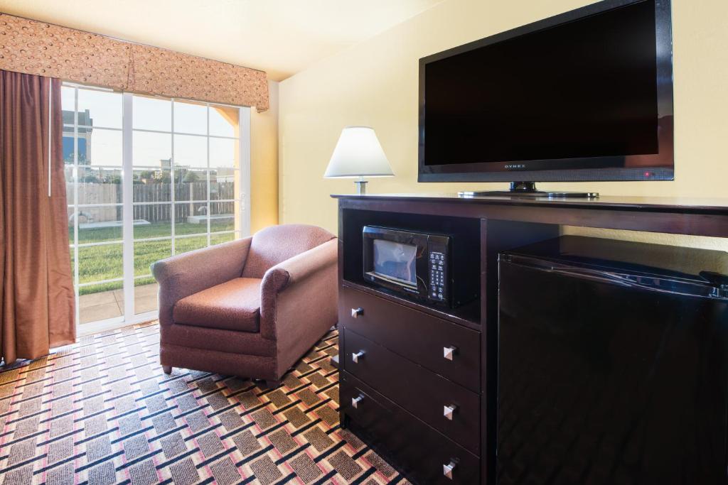 a hotel room with a flat screen tv and a chair at Days Inn by Wyndham Joplin in Joplin