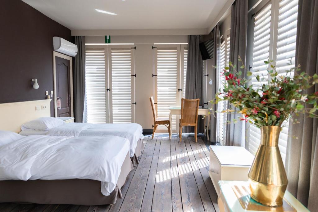 a bedroom with two beds and a table with a vase of flowers at Thermae Grimbergen Hotel in Grimbergen